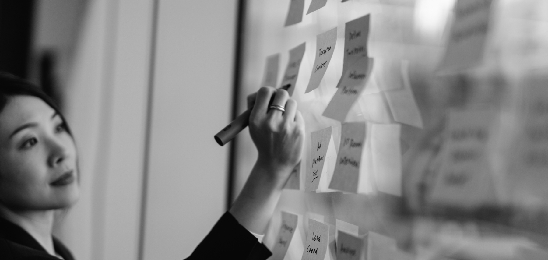 A woman writing on a wall with post it notes.