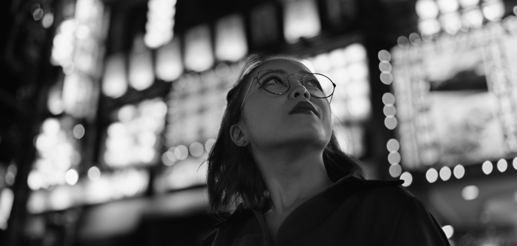 A black and white photo of a woman in glasses looking up.
