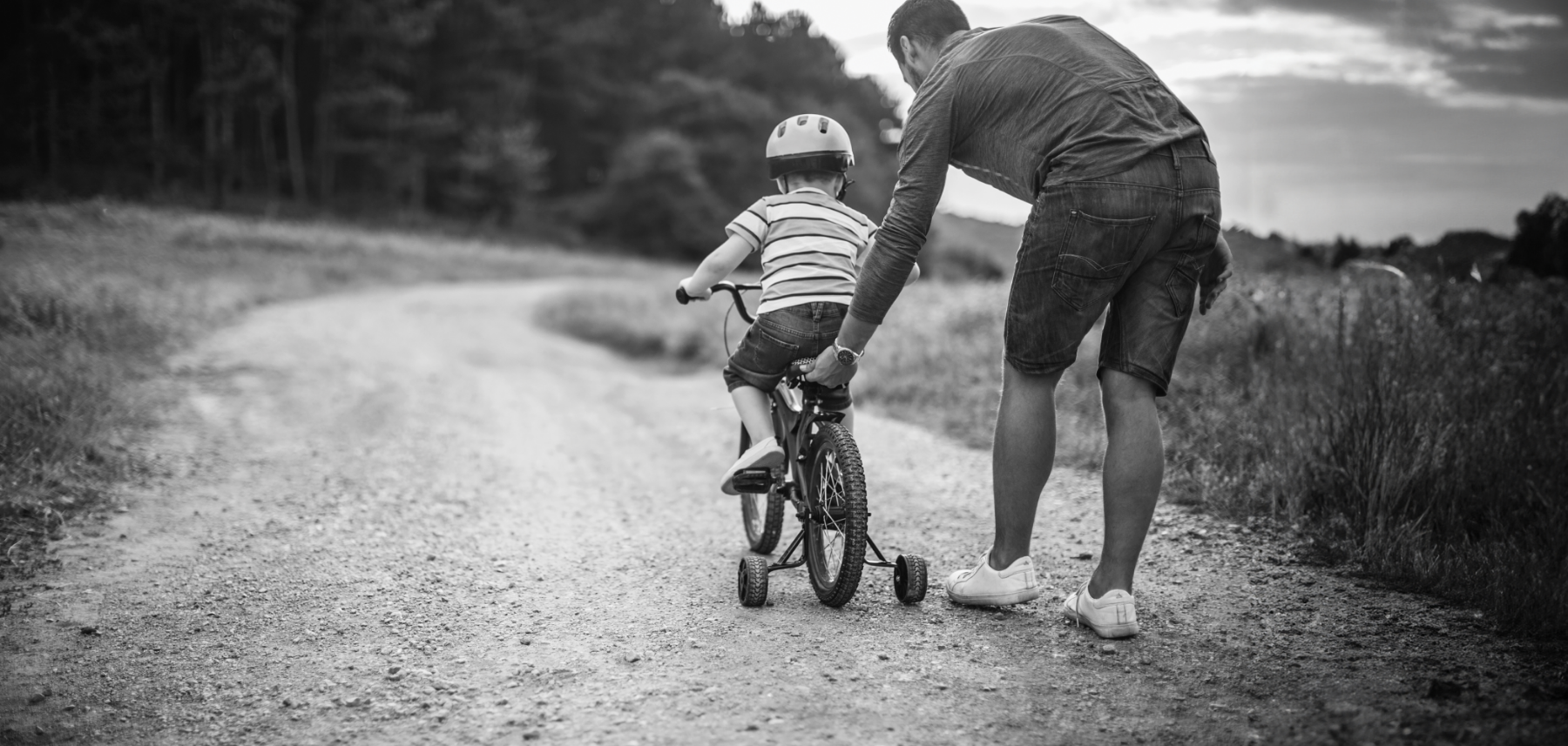A man and a child riding a bicycle on a dirt road.