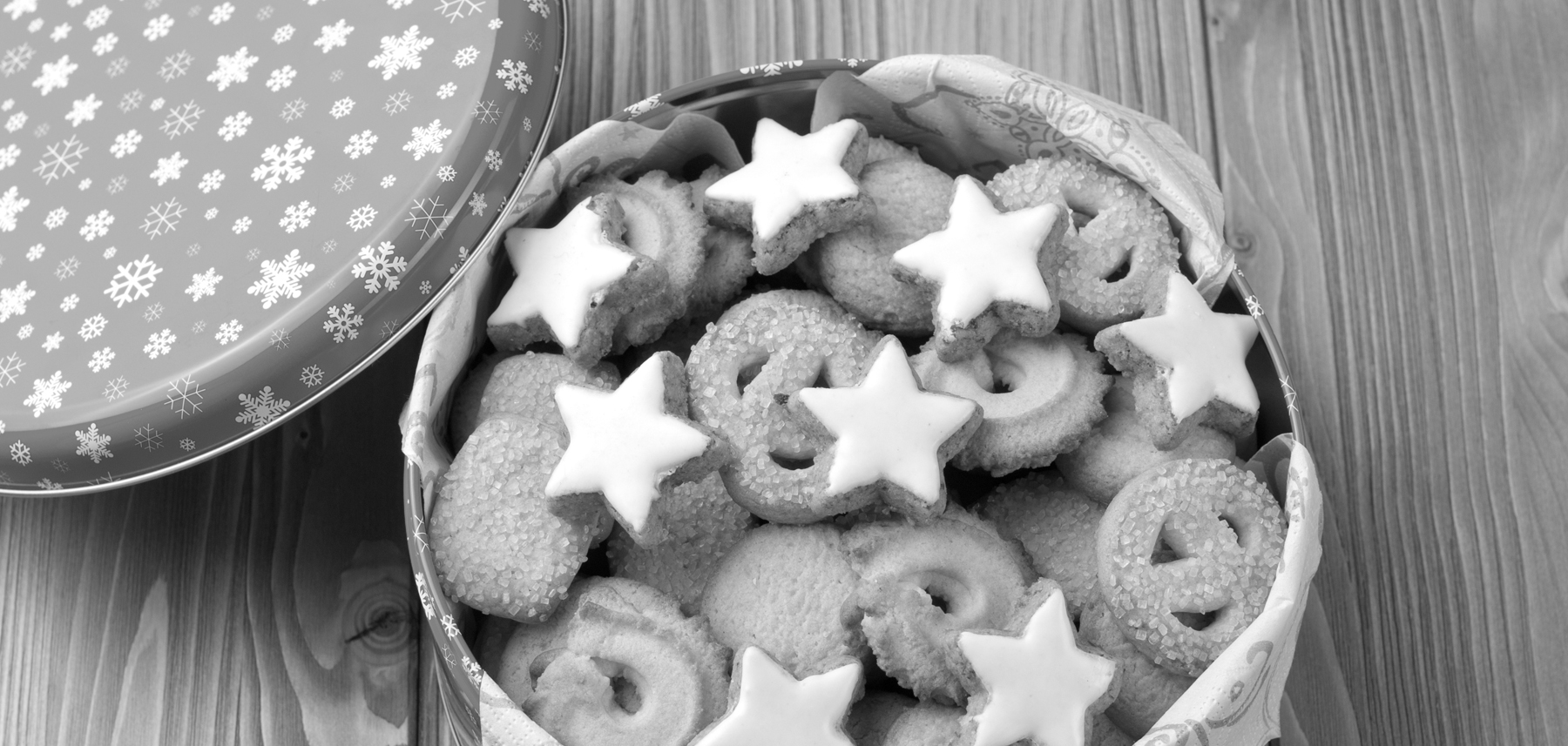 A tin of assorted christmas cookies on a wooden surface.