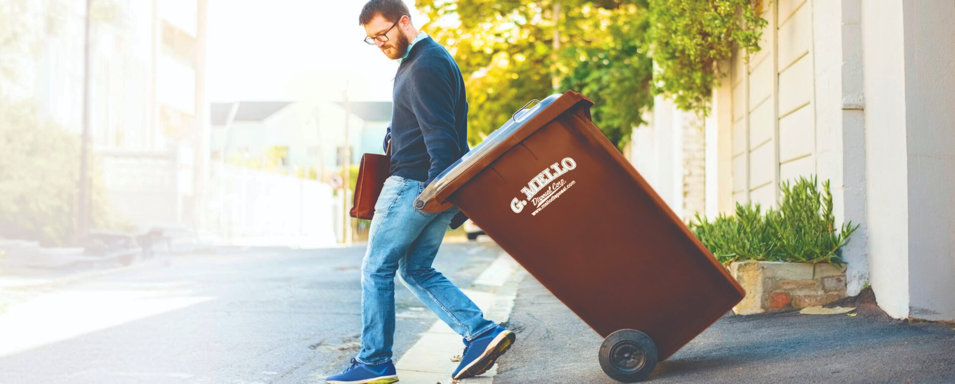Man taking his G. Mello Disposal Corp trash can to the curb